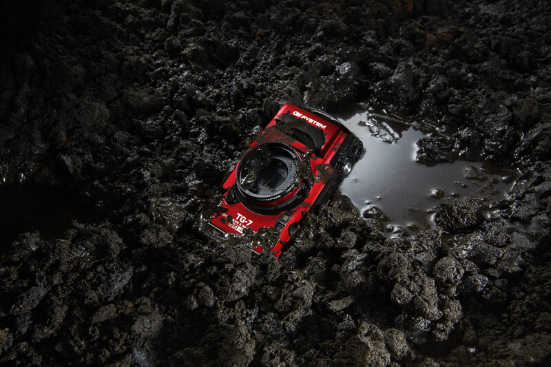 Red digital camera positioned on dark rocky terrain next to a small pool of water.