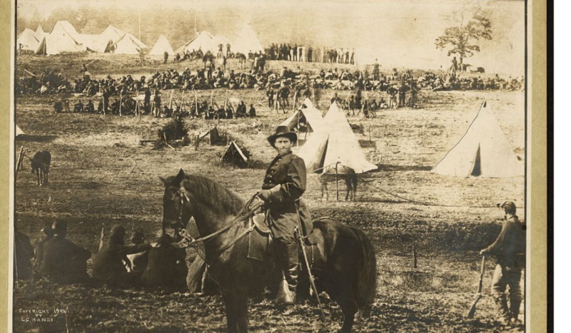 Cavalry soldier on horseback at a military encampment with numerous canvas tents in the background.