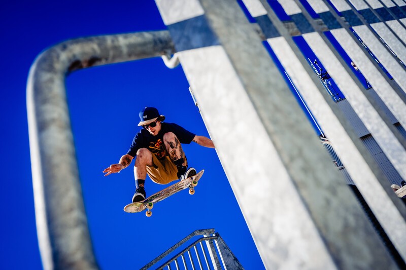 Skateboarder performing aerial trick against clear blue sky with geometric concrete structure.