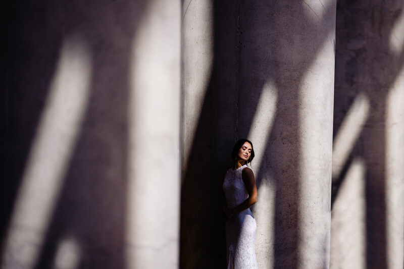 Woman in white dress standing between dramatic shadow lines cast on a textured wall.