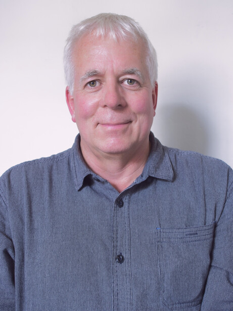 Portrait of a middle-aged man with gray hair wearing a blue button-up shirt against a plain light background.