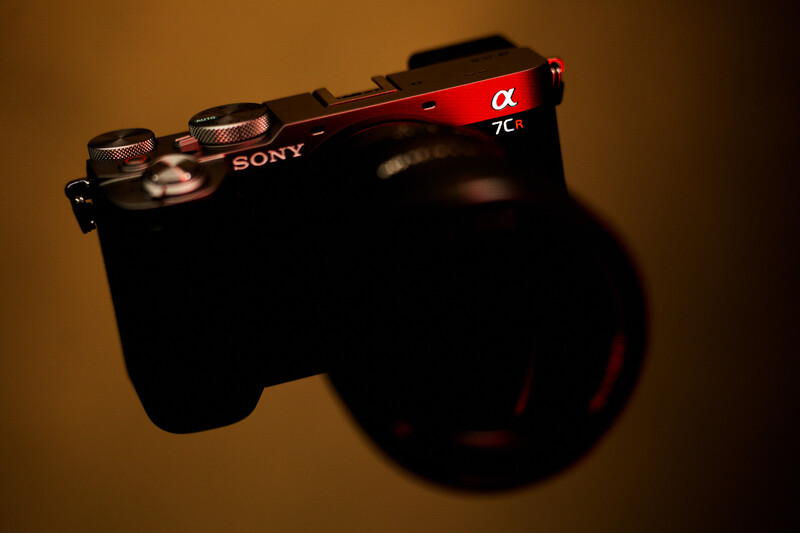 Sony α7c mirrorless camera positioned at an angle against a warm, blurred background with dramatic lighting and shadow.