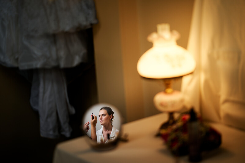 A woman's face appearing inside a snow globe on a table, with a vintage lamp glowing softly in the background.