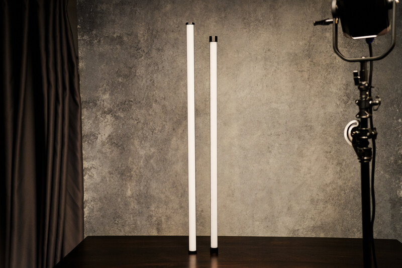 Two vertical fluorescent tubes illuminated against a textured studio backdrop with professional lighting setup.