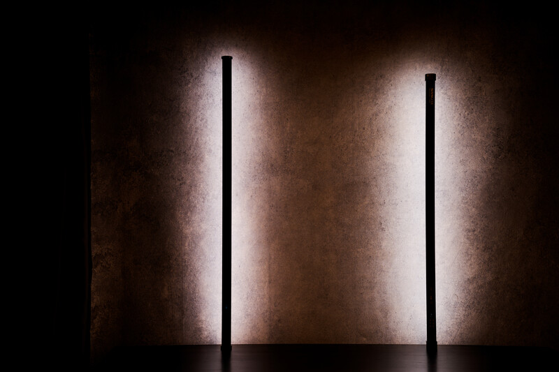 Two vertical neon tubes with glowing halos against a textured concrete wall.