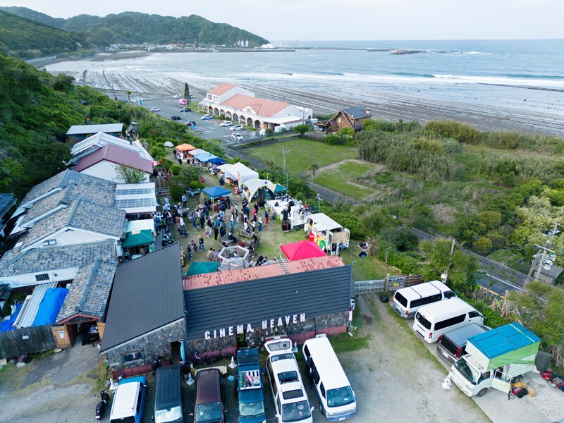 Aerial view of an outdoor cinema event setup on a grassy hillside overlooking a beach and ocean.