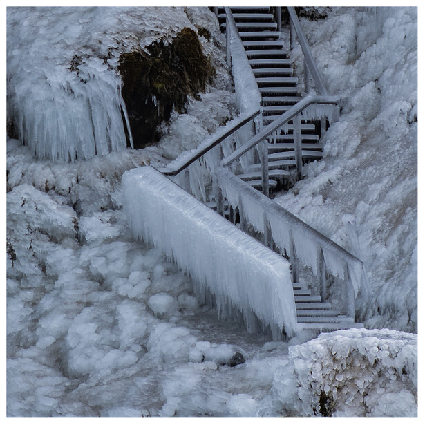 Frozen staircase and handrails encased in thick icicles descending a snowy hillside.