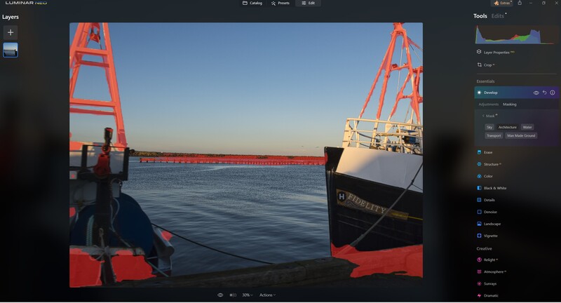 Large red industrial crane and cargo ship viewed from a smaller vessel on calm water.