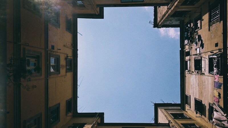 Upward view of terracotta buildings framing a clear blue sky in a narrow urban courtyard.
