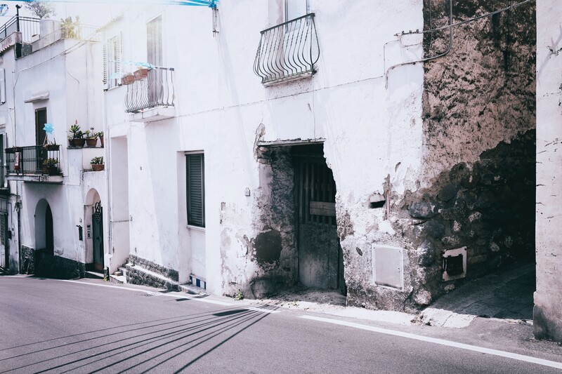 Weathered white-walled Mediterranean building with dark doorway and metal balconies.