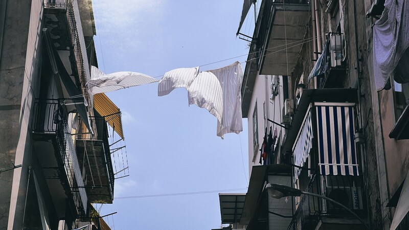 White laundry hanging between buildings in a narrow urban alley against blue sky.