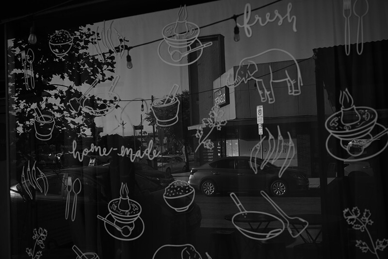 Window display with hand-drawn food illustrations in white chalk on black glass, including bowls, pans, and utensils with "home-made" text.