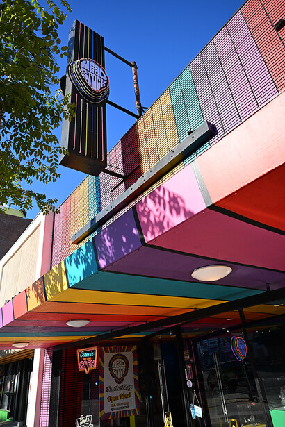 Colorful retro storefront with neon signs and stacked shipping containers under blue sky.