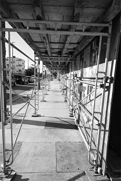 Black and white photograph of a long corridor beneath an elevated structure with metal railings and support beams.
