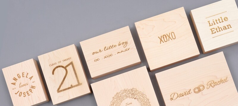 Wooden tiles with engraved text and designs arranged on a gray surface, including names, dates, and decorative patterns.