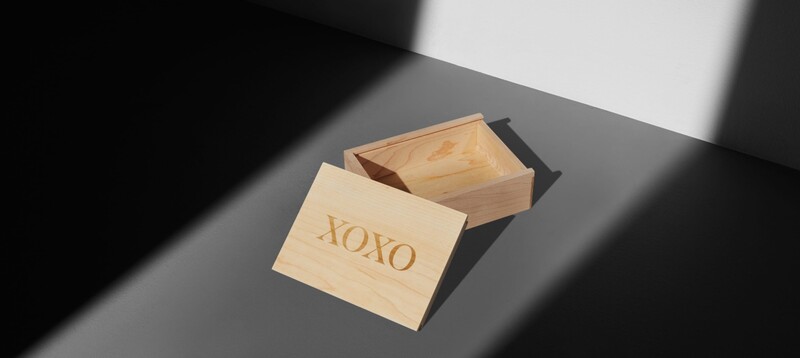 Wooden box with engraved "XOXO" text, partially open on gray surface with dramatic shadow.