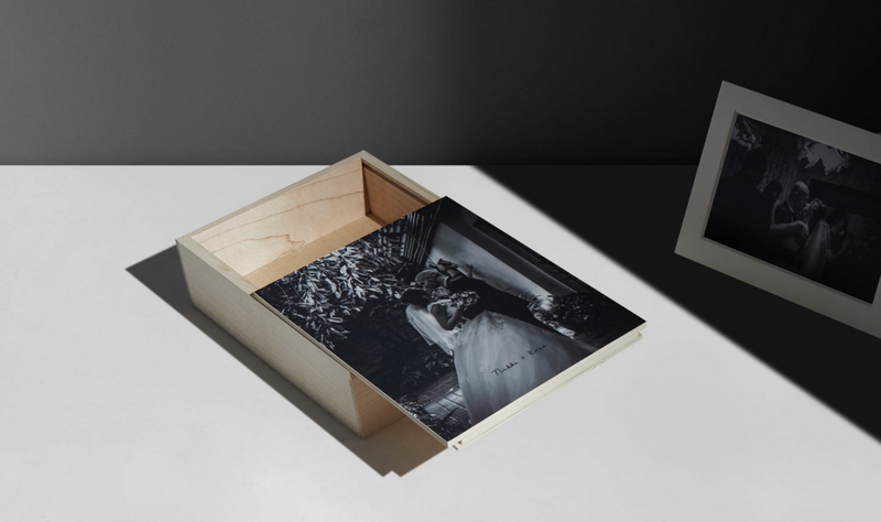 Wooden box containing a black and white photograph, displayed on white surface with studio lighting and framed print in background.