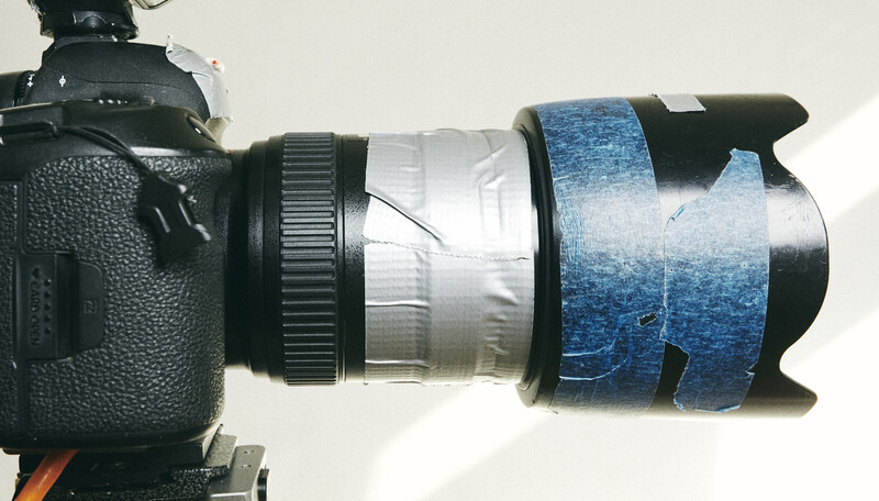 DSLR camera with standard lens wrapped in blue gaffer tape and white tape for protection or labeling.