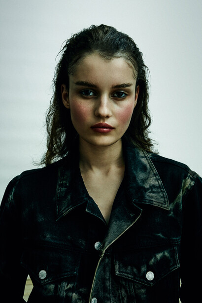 Young woman in dark denim jacket against neutral white background, direct gaze at camera.