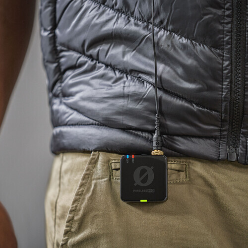 Compact black portable device hanging from beige pants pocket with lanyard against dark puffy jacket.