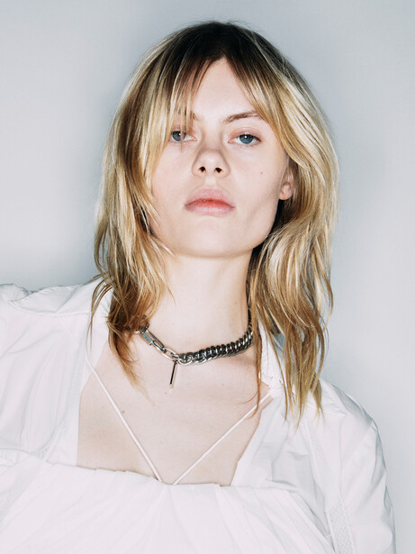 Portrait of a young woman with blonde hair and bangs wearing a white button-up shirt.