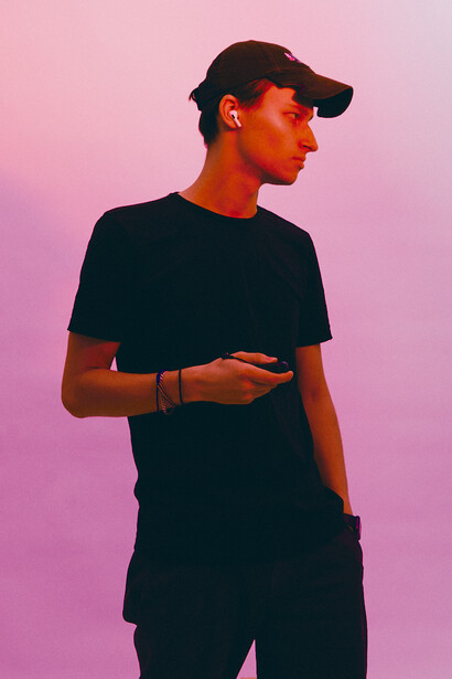 Person wearing black cap and t-shirt against pink gradient background, looking to the side.