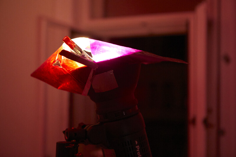 Studio light fixture with red and magenta gels creating warm and cool color temperature contrast against a shadowed doorway.