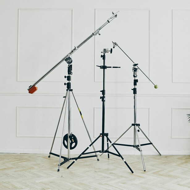 Professional lighting and grip equipment setup with boom arm, light stands, and reflectors against white wall.