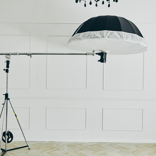 Studio lighting setup with umbrella reflector mounted on boom arm and tripod-mounted key light.