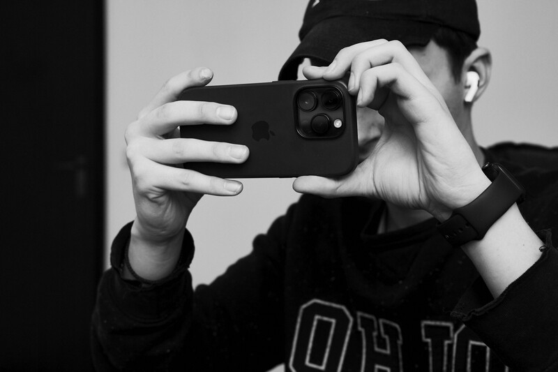 Person in black clothing holding smartphone horizontally to frame a shot, shown in high-contrast black and white.