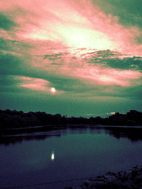 Sunset reflecting on still water with pink and green clouds above a dark shoreline.