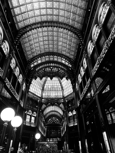 Black and white photograph of an ornate covered arcade with barrel-vaulted glass ceiling and symmetrical archways.