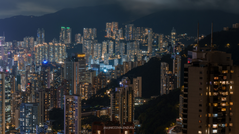 Dense urban skyline at dusk with illuminated high-rise buildings against dark mountains.