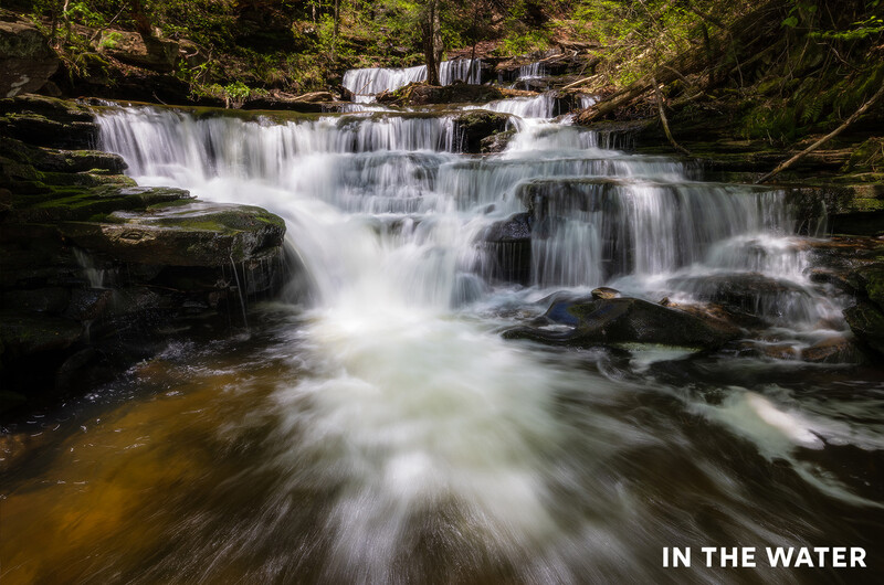 Cascading waterfall flowing over tiered rock formations surrounded by dense forest.