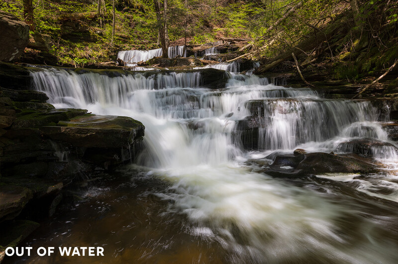 Multi-tiered waterfall cascading through a forested stream with silky water effect.