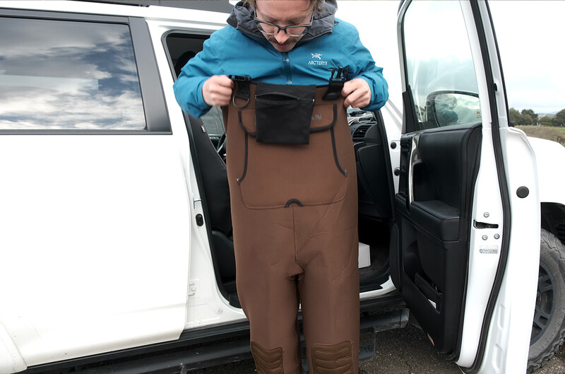 Person in blue jacket holding up brown waders next to a white van.