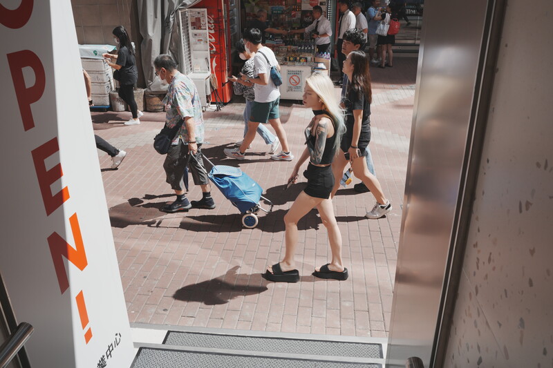 Street scene photographed through a storefront window showing people exercising outdoors on a sunny day.