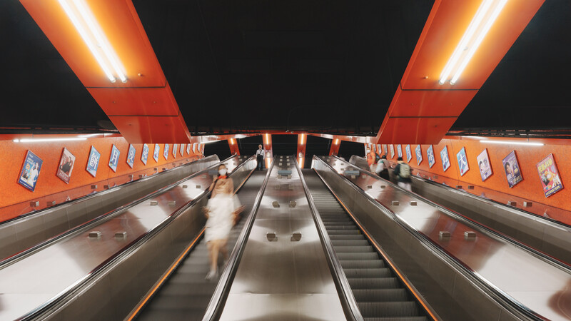 Symmetrical perspective view down an escalator with bright orange walls and recessed lighting against a dark ceiling.