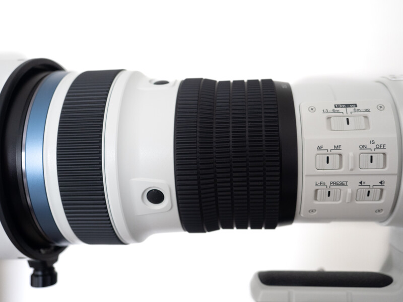White telephoto lens with focus ring and control buttons displayed against white background.