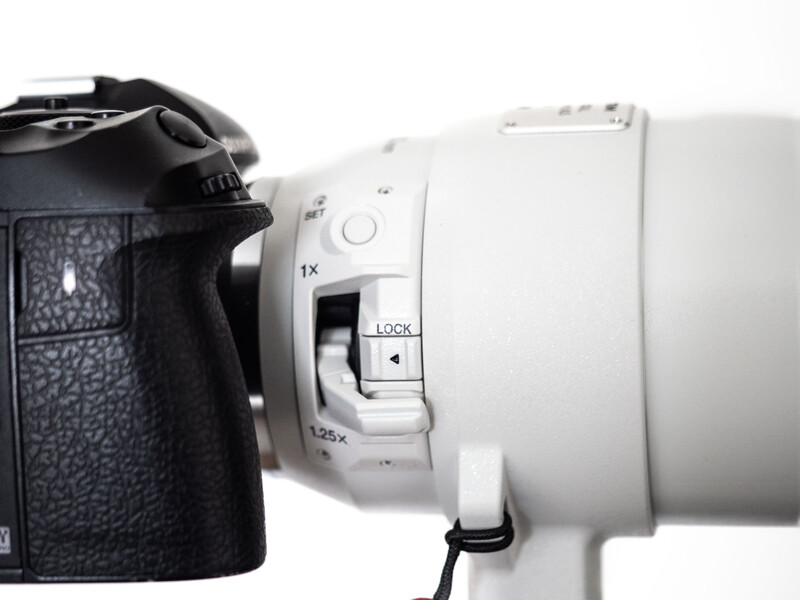 Close-up of a white telephoto lens mounted on a black camera body against white background.