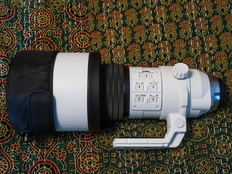 White telephoto lens with black grip and control ring displayed on patterned fabric.