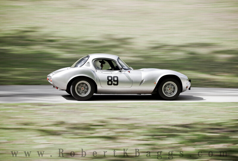 White vintage race car with number 89 on its side moving at speed, captured with motion blur of surrounding landscape.