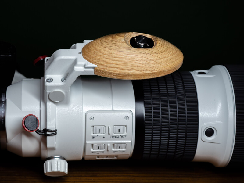 White underwater camera housing with wooden grip ball and black rubber focus ring against black background.