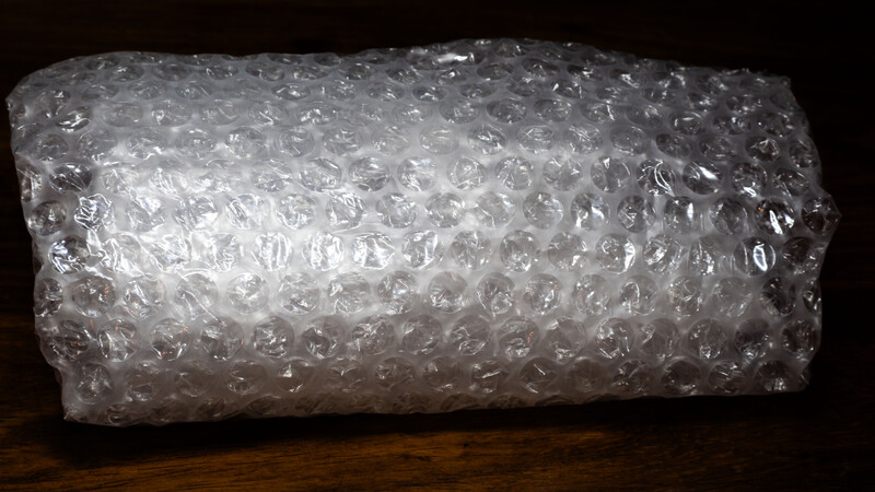 Roll of bubble wrap with clear plastic bubbles photographed against a dark wooden surface and black background.