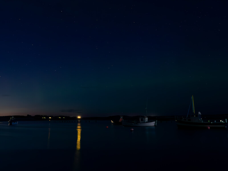 Twilight harbor scene with moored sailboats silhouetted against a darkening blue sky and calm water.