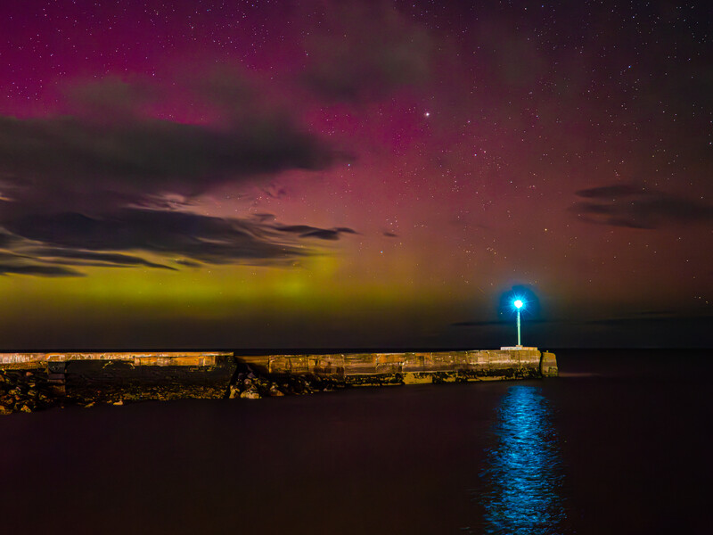 Illuminated lighthouse beacon glowing blue against a twilight sky with magenta and yellow clouds.
