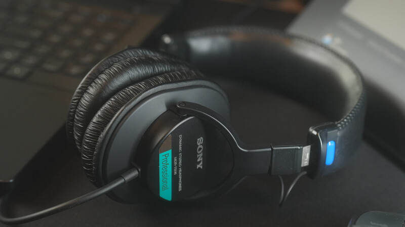 Sony professional headphones with a teal label resting on a desk near a keyboard and laptop.