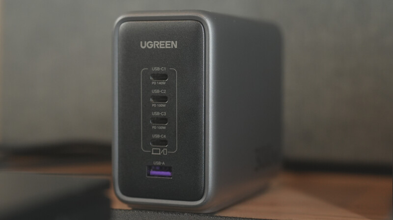Ugreen multi-port USB charging hub with dark gray casing and labeled ports displayed on wooden surface.