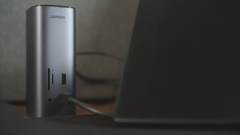 Silver cylindrical power bank with USB ports sitting next to a laptop on a wooden surface.