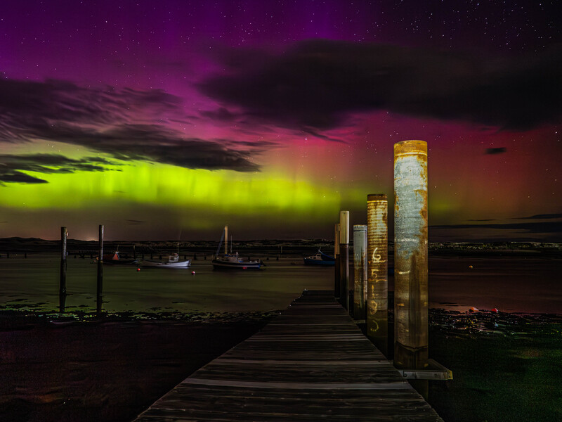 Wooden pier extending into dark water under a dramatic purple and lime-green sky at dusk.